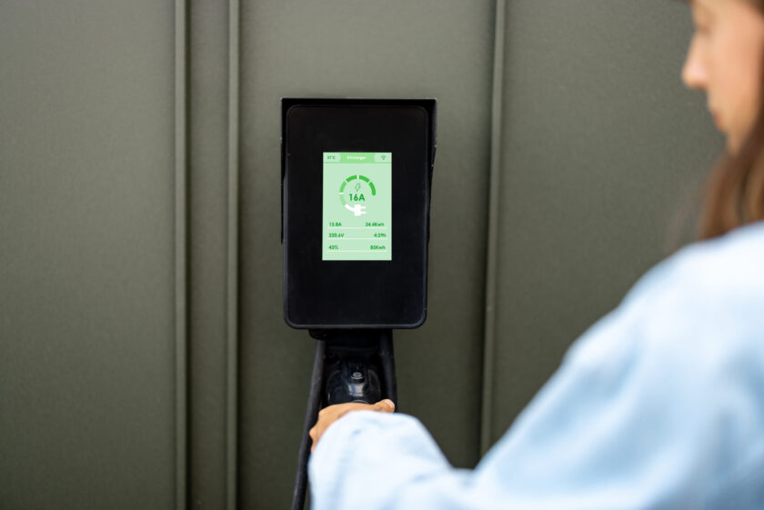 Woman takes a plug of a charging wall station with a touch screen for charging electric cars, close-up. Concept of modern technologies