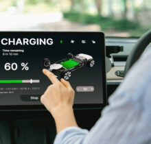 Young woman inside the vehicle, checking EV vehicle's application on battery recharging electricity status display on smart monitor screen in modern EV car on her road trip journey. Exalt